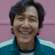 Seong Gi-hun in Squid Game, smiling for the camera.